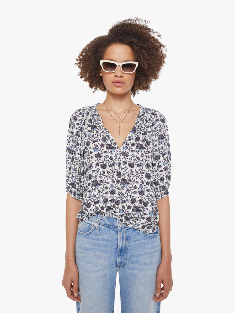 Front view of a woman in a white and navy floral print top with a V-neck, elbow-length sleeves, buttons down the front and a loose fit.
