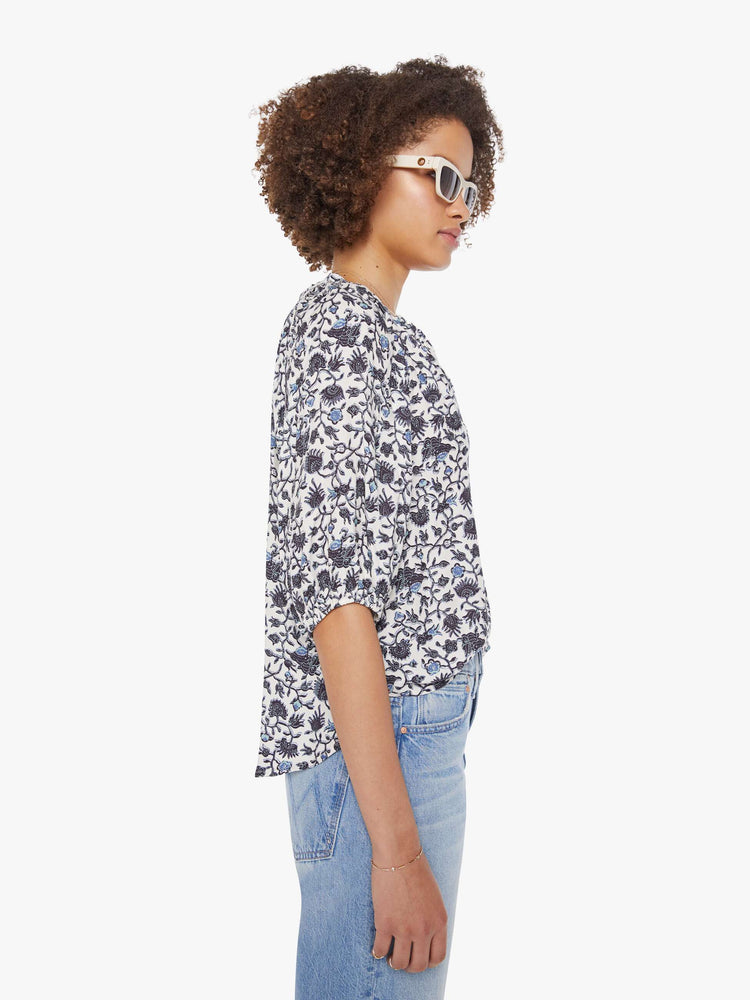 Side view of a woman in a white and navy floral print top with a V-neck, elbow-length sleeves, buttons down the front and a loose fit.