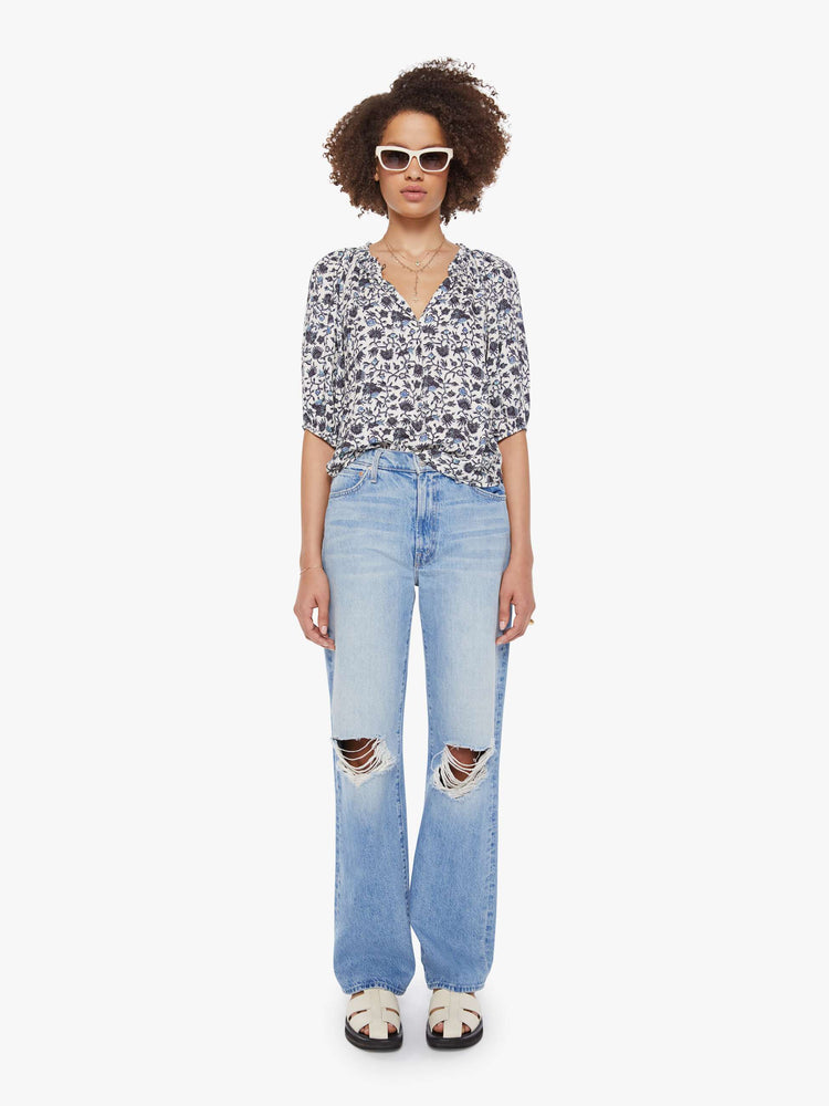 Full body view of a woman in a white and navy floral print top with a V-neck, elbow-length sleeves, buttons down the front and a loose fit.