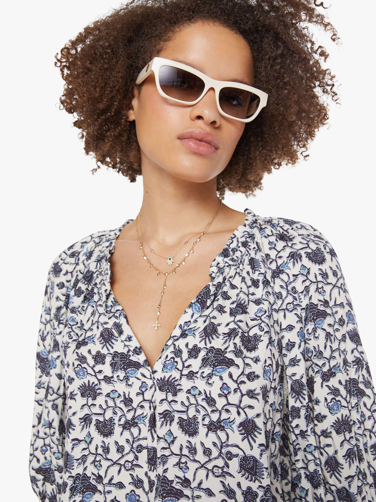 Close up view of a woman in a white and navy floral print top with a V-neck, elbow-length sleeves, buttons down the front and a loose fit.