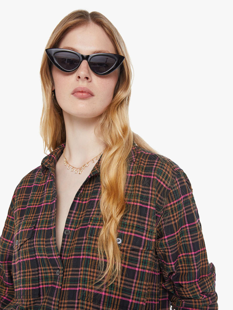 Close up view of a woman in brown plaid dress has a collared neckline, elbow-length sleeves, buttons down the front and a loose, boxy fit.