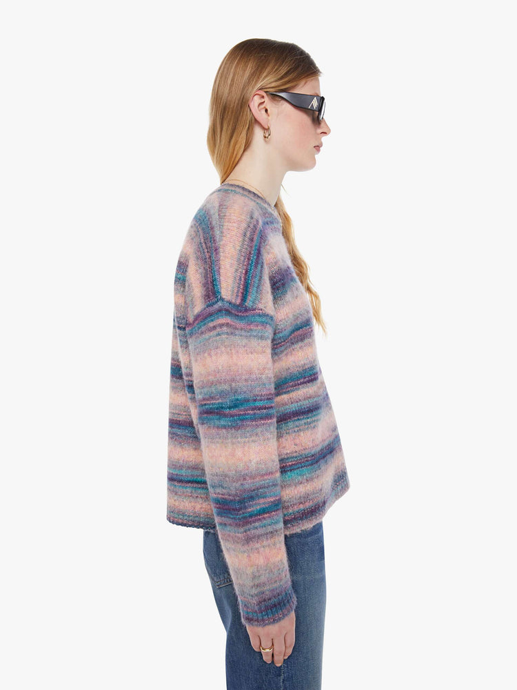 Side view of a woman in a pink and blue stripes the long-sleeve sweater with drop shoulders and an oversized fit.