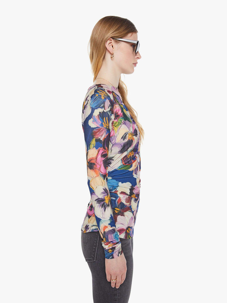 Side view of a woman in an abstract flower top with a crewneck that drapes across the chest and gathered side seams for a ruched look.