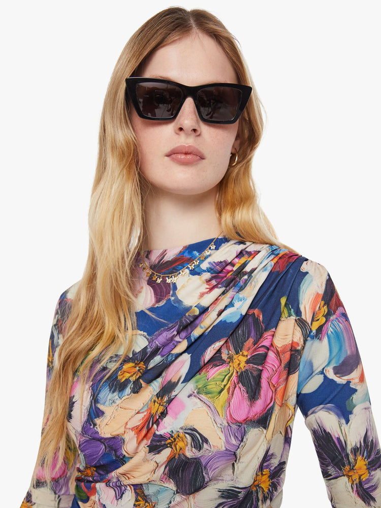 Close up view of a woman in an abstract flower top with a crewneck that drapes across the chest and gathered side seams for a ruched look.