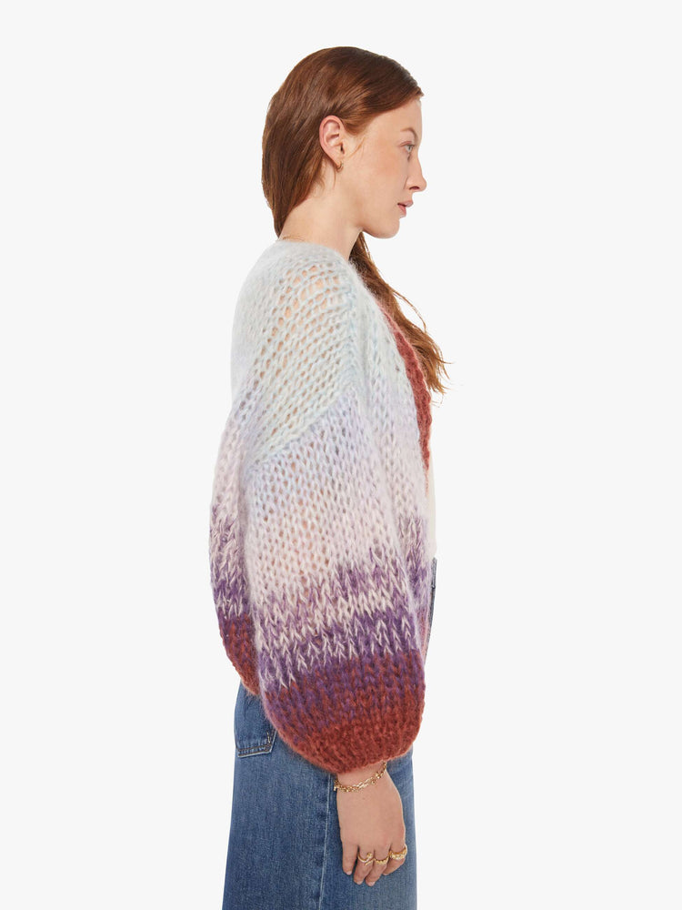 Side view of a woman in a  hand knit from a soft blend of mohair and wool in a light blue and purple gradient pattern with burgundy trim cardigan.