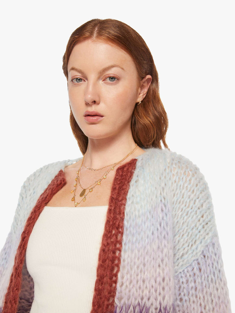 Close up view of a woman in a  hand knit from a soft blend of mohair and wool in a light blue and purple gradient pattern with burgundy trim cardigan.