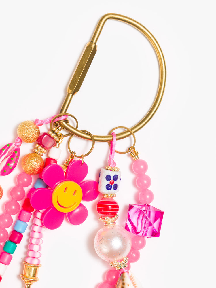 Clasp view of a bag charm with mixed beads in shades of pink, shells, dice beads and a smiling flower.