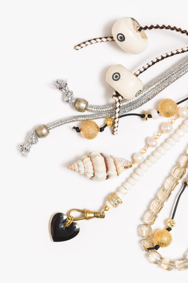 Close up view of a bag charm with mixed beads in shades of black, white and gold, with heart and mushroom charms. 