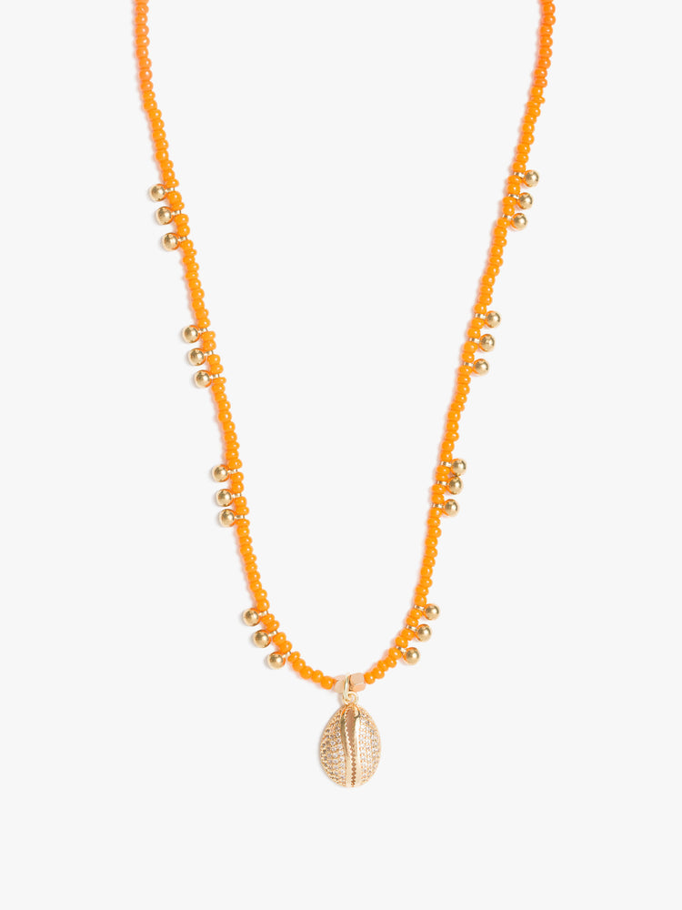 View of a beaded necklace features orange seed beads, brass balls and a gold-plated shell charm.