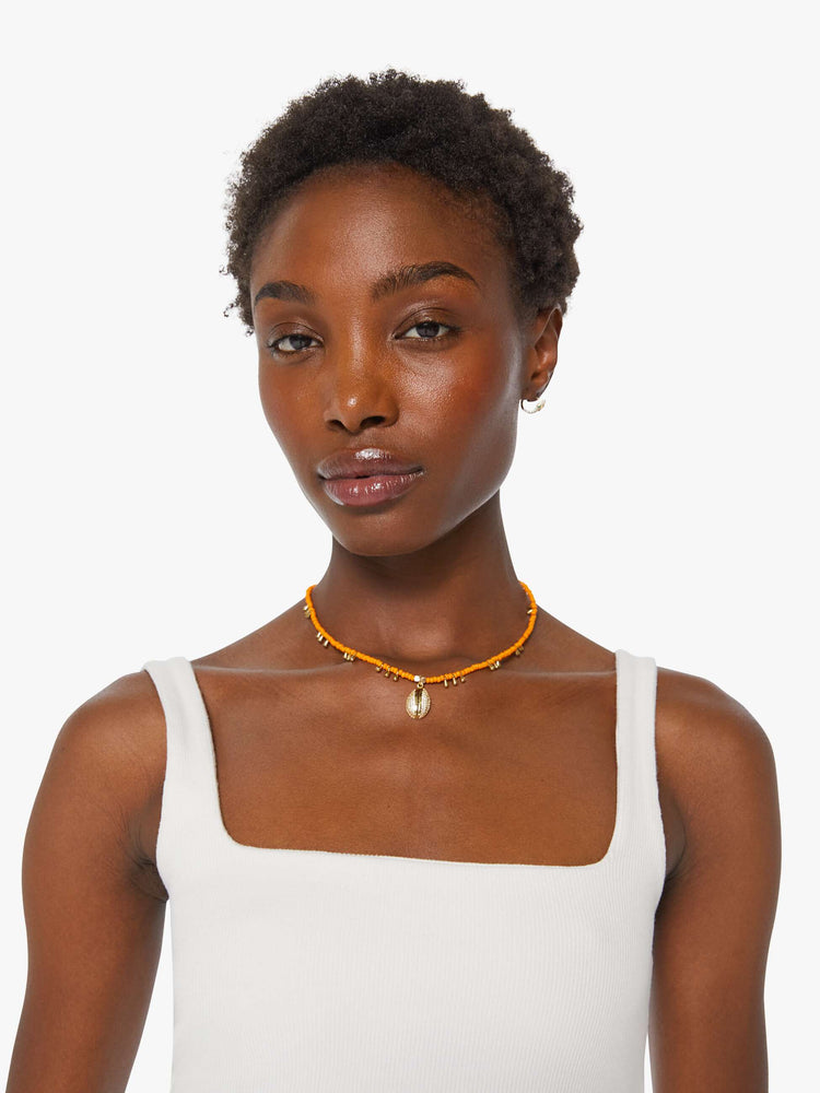 On model of view of beaded necklace features orange seed beads, brass balls and a gold-plated shell charm.
