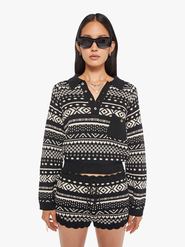 Front view of a woman in a black and off-white  top cable knit-inspired design, and features a buttoned V-neck, a front patch pocket, ribbed hems and a cropped fit.