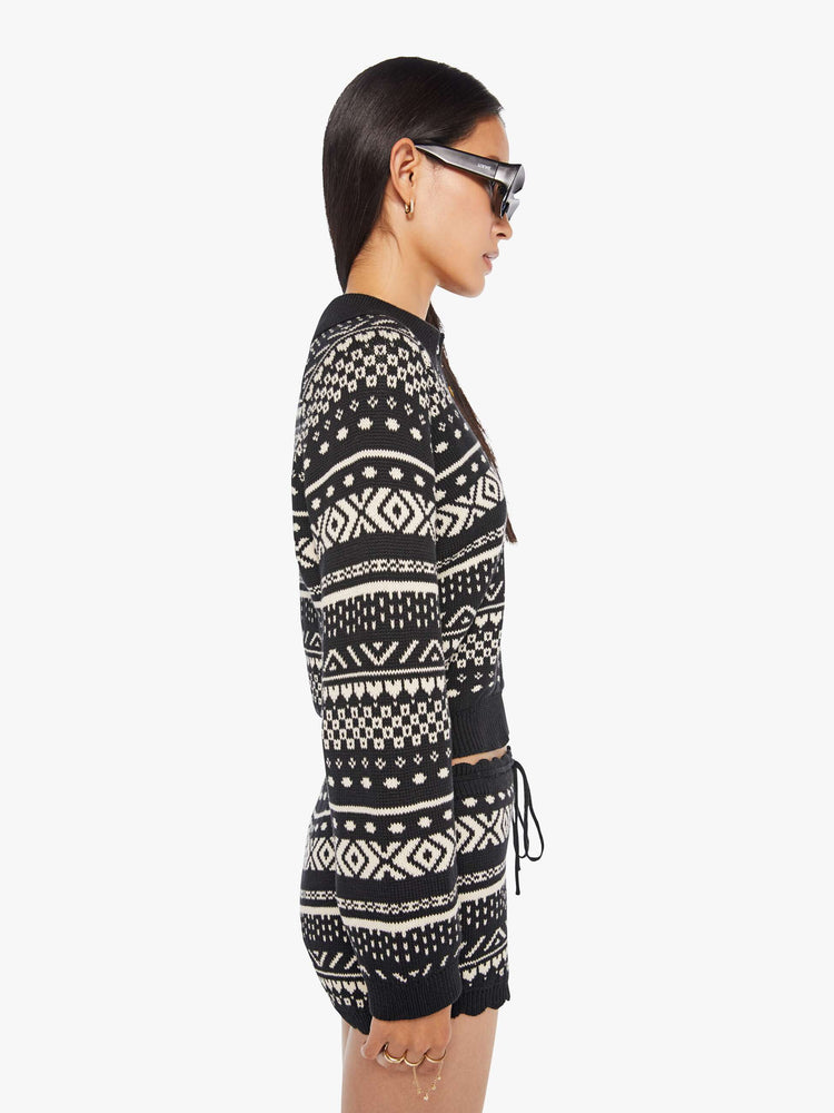 Side view of a woman in a black and off-white  top cable knit-inspired design, and features a buttoned V-neck, a front patch pocket, ribbed hems and a cropped fit.