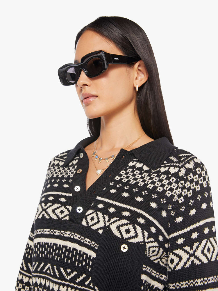 Close up view of a woman in a black and off-white  top cable knit-inspired design, and features a buttoned V-neck, a front patch pocket, ribbed hems and a cropped fit.