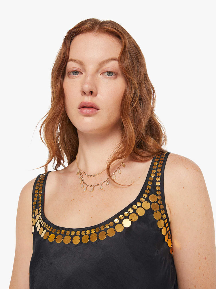 Close up view of a woman in a  black tank with gold beaded details along the neck and sleeves, and features a deep scoop neck and a cropped boxy fit.