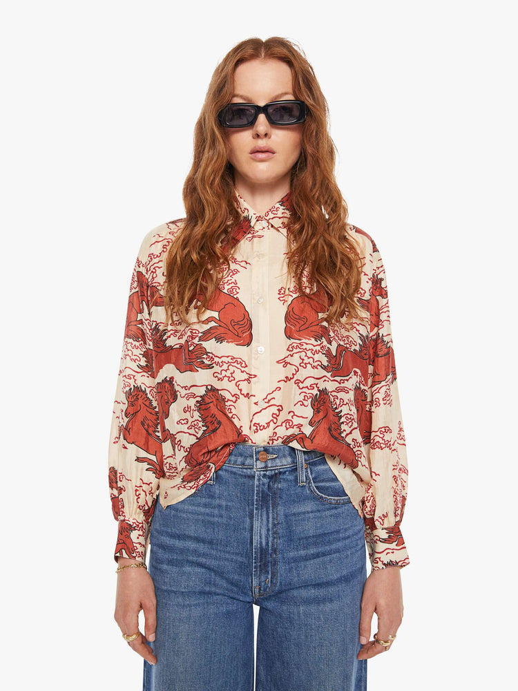 Front view of a woman in a cream shirt with a maroon Pegasus print, and features drop shoulders, long sleeves, curved hems and buttons down the front.