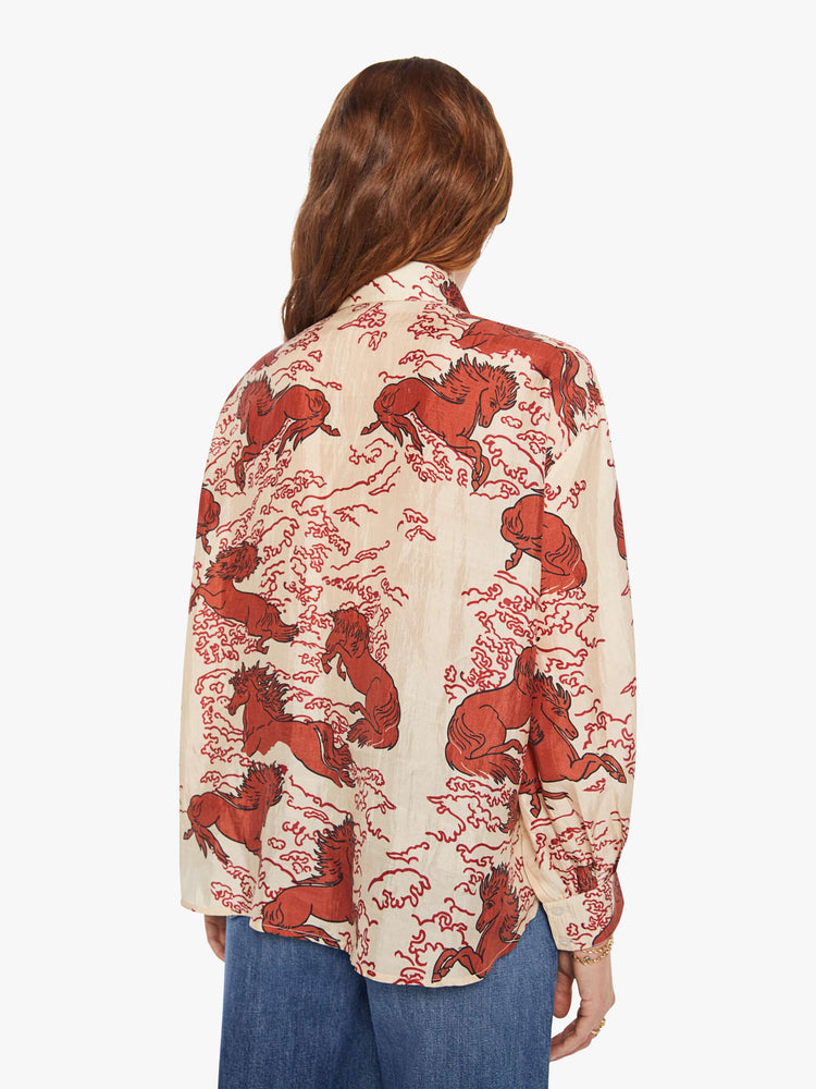 Back view of a woman in a cream shirt with a maroon Pegasus print, and features drop shoulders, long sleeves, curved hems and buttons down the front.