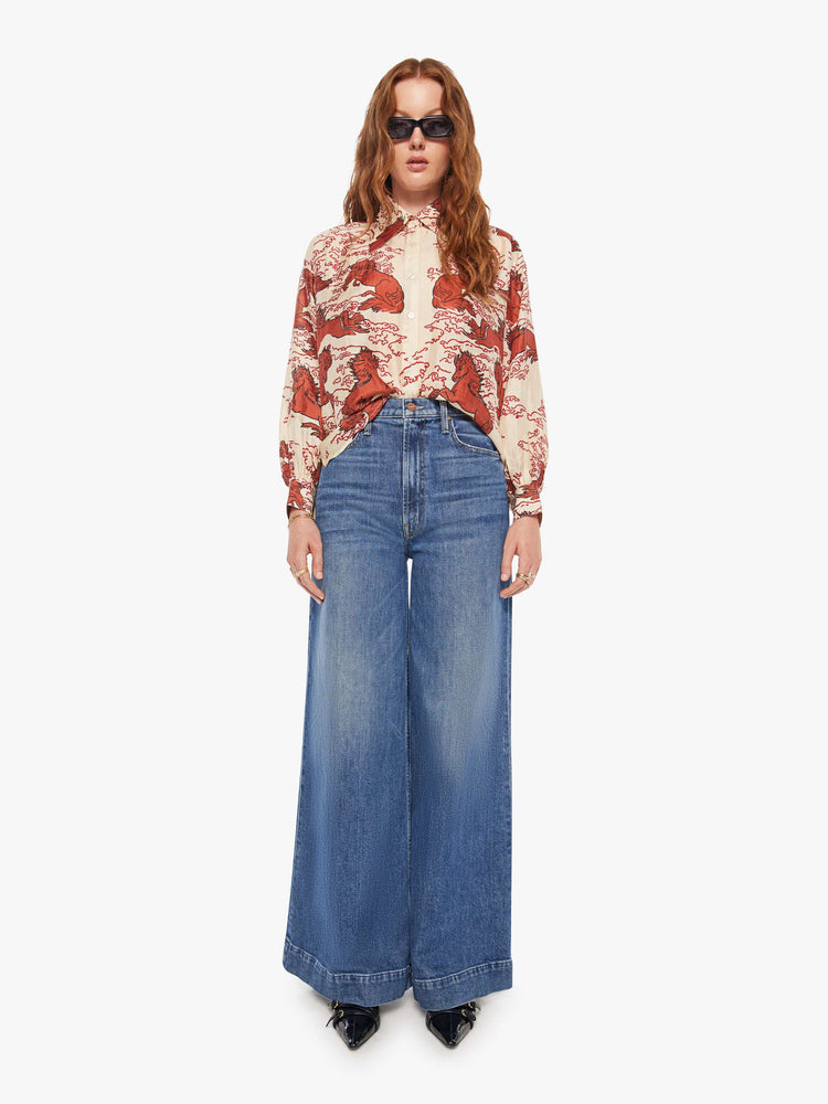 Full body view of a woman in a cream shirt with a maroon Pegasus print, and features drop shoulders, long sleeves, curved hems and buttons down the front.