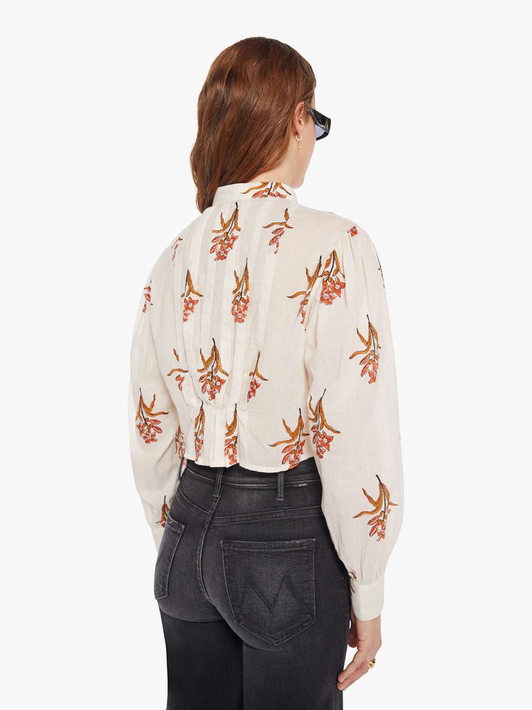 Back  view of a woman in a off-white shirt with a delicate floral print, and features a crewneck, pleats along the shoulder, long balloon sleeves, a cropped fit and buttons down the front.