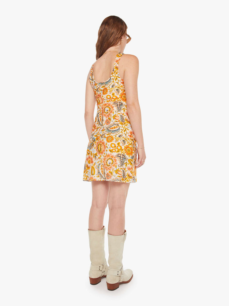 Back view of a woman in a mini sleeveless dress in an orange and yellow paisley print, and features a scoop neck, narrow fit and short hem.