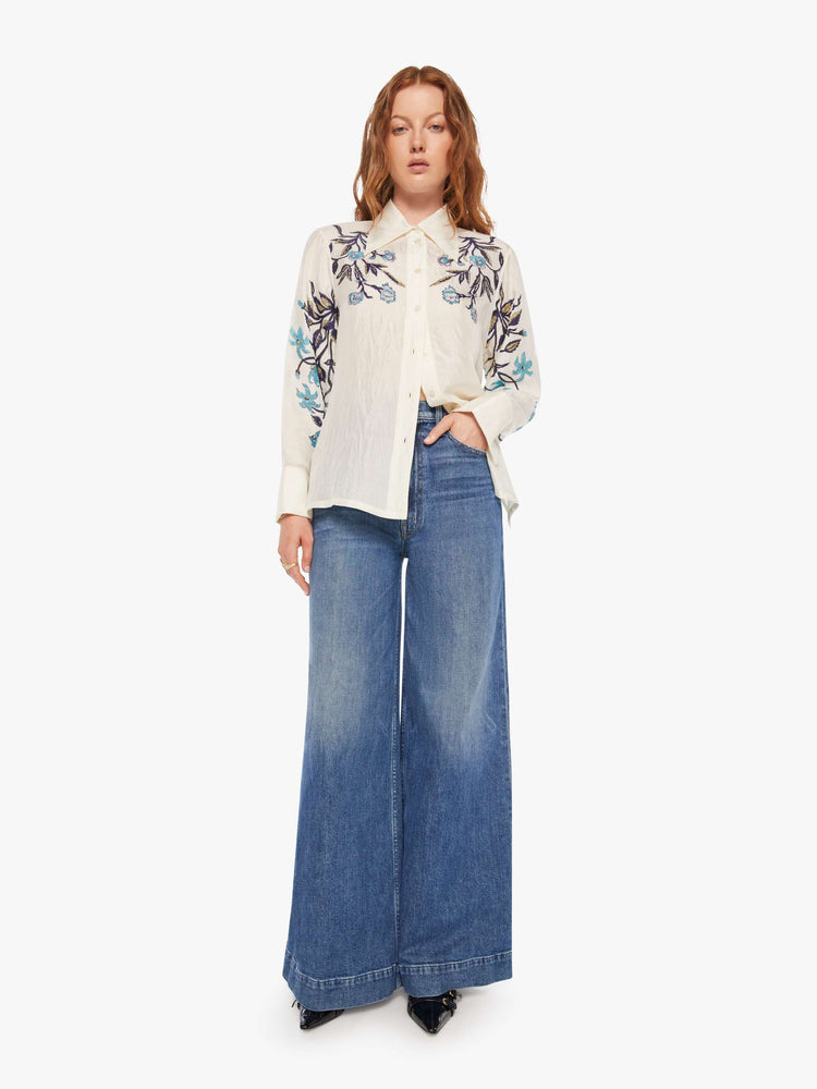 Full body view of a woman in an off-white shirt with blue lilies across the chest and sleeves, and features long balloon sleeves and a loose fit.