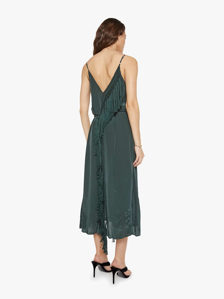 Back view of a woman in a dark green dress designed with thin spaghetti straps, a deep V-neck, fringed trim and a flowy fit.