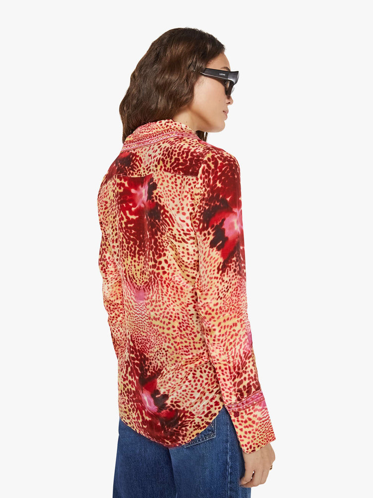 Back view of a woman in a top with abstract pink floral print with a V-neck, long sleeves and a narrow fit.