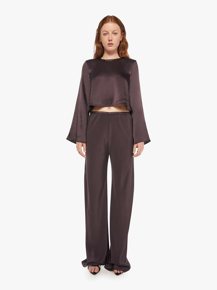 Front view of a woman in dark brown pants with a high rise and a loose straight leg. 