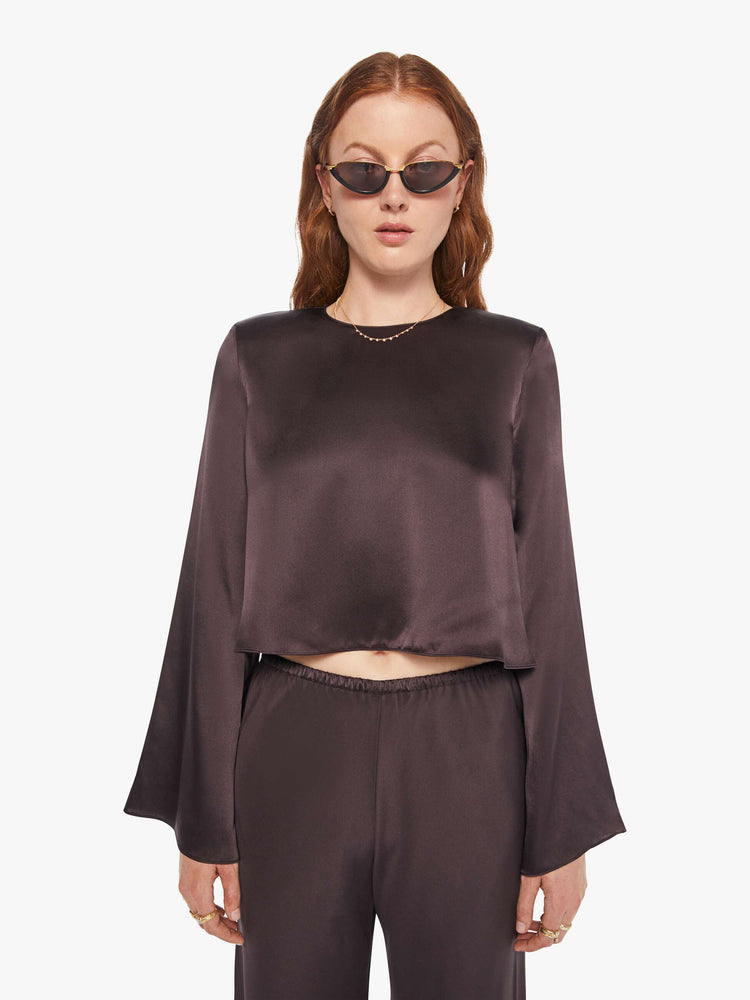 Front view of a woman in a oak brown color blouse with long bell sleeves, a cropped hem and loose fit.