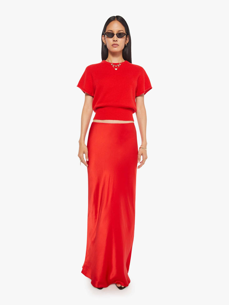 Front view of a woman in a red bias cut maxi skirt is designed with a straight fit and a flowy ankle-grazing hem.