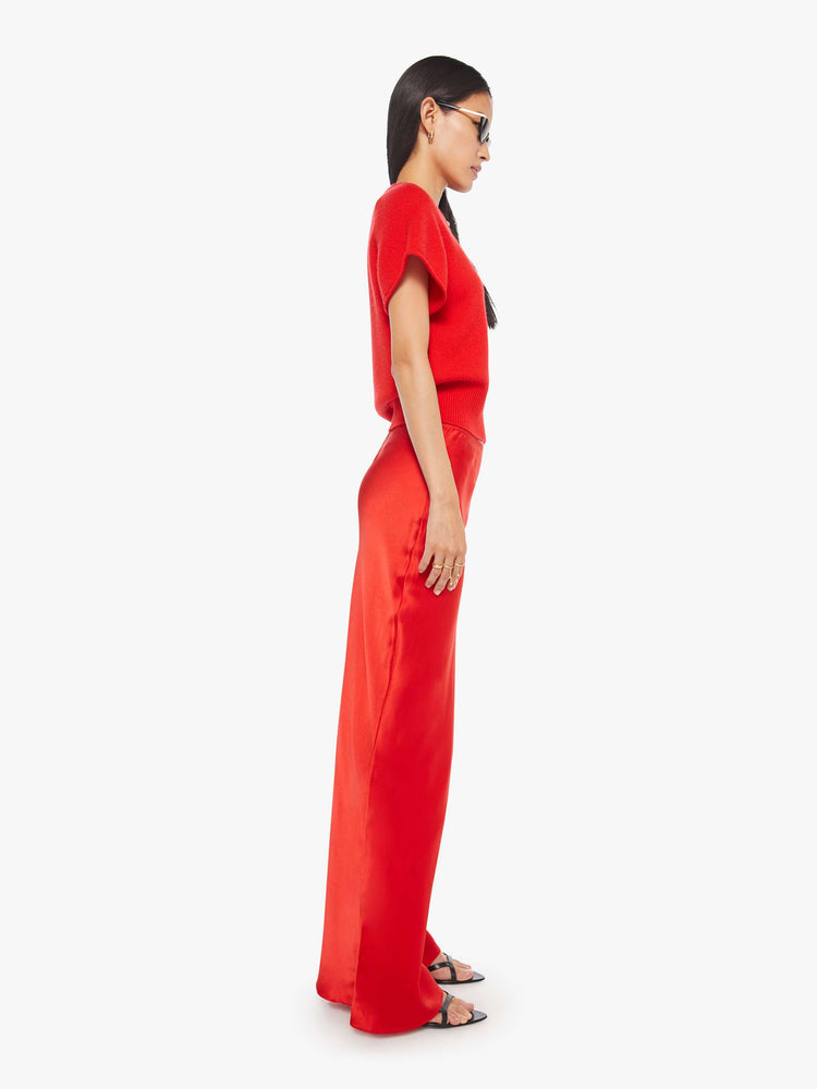 Side view of a woman in a red bias cut maxi skirt is designed with a straight fit and a flowy ankle-grazing hem.