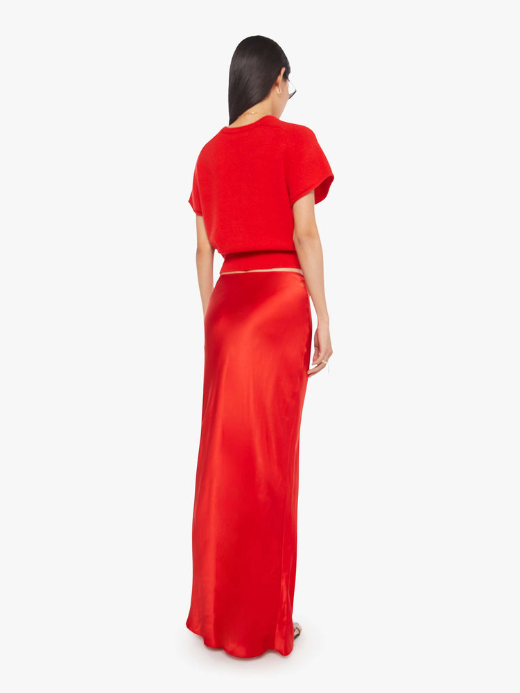 Back view of a woman in a red bias cut maxi skirt is designed with a straight fit and a flowy ankle-grazing hem.