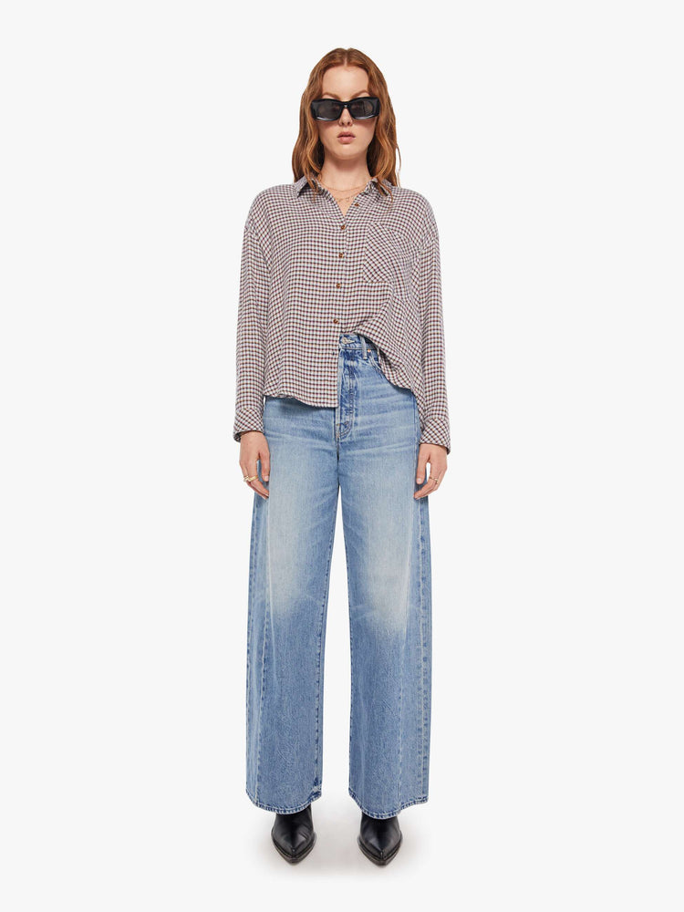 Full body view of a woman in a white and baby blue checker print long sleeve shirt is designed with drop shoulders, a front patch pocket, curved hem and slightly cropped fit.