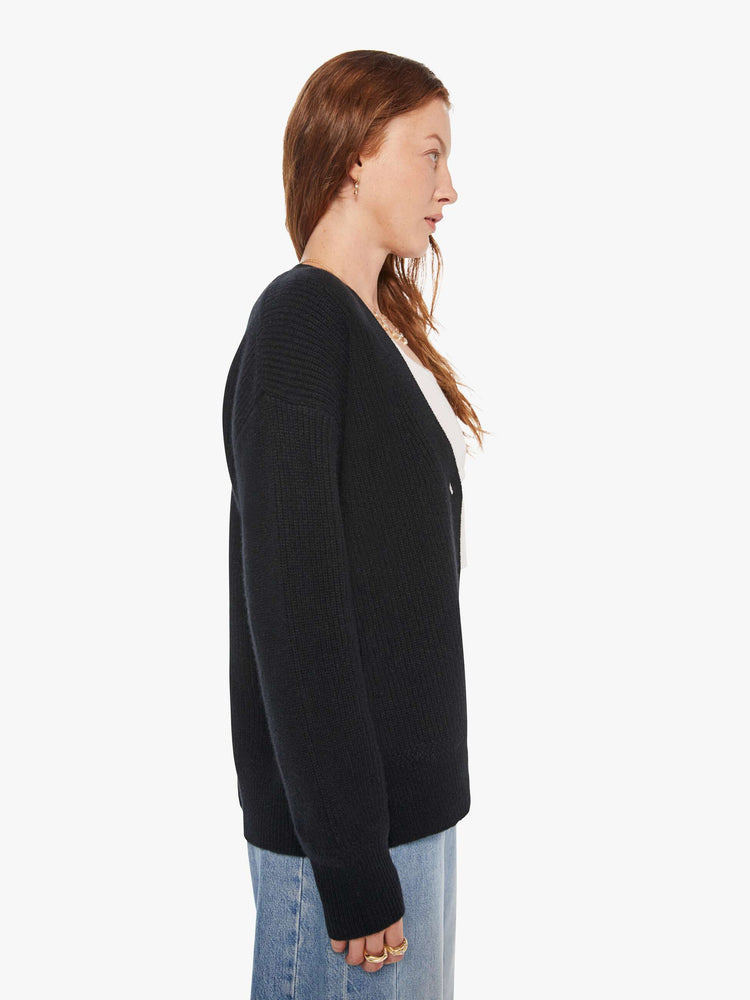 Side view of a woman in a black cardigan has a deep V-neck, drop shoulders, buttons down the front and ribbed hems.