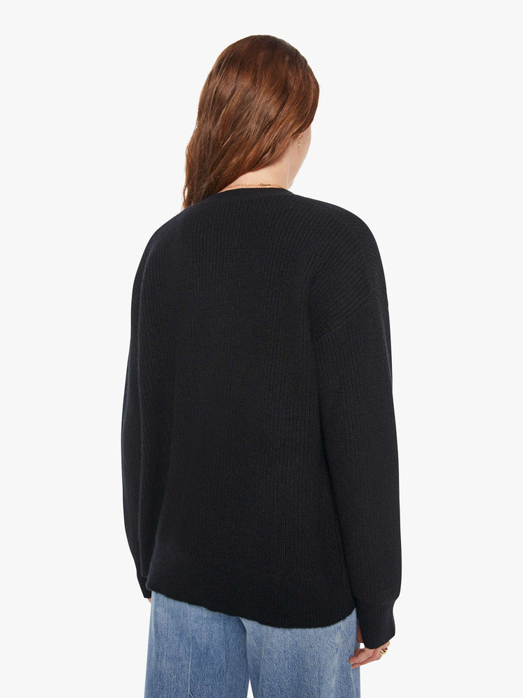 Back view of a woman in a black cardigan has a deep V-neck, drop shoulders, buttons down the front and ribbed hems.