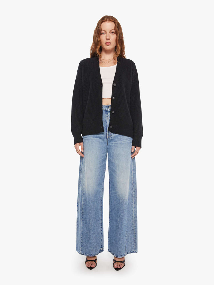 Full body view of a woman in a black cardigan has a deep V-neck, drop shoulders, buttons down the front and ribbed hems.