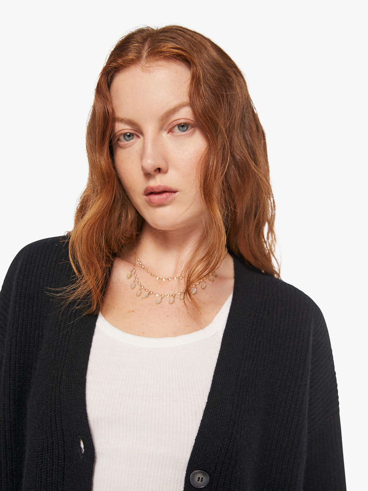 Close up view of a woman in a black cardigan has a deep V-neck, drop shoulders, buttons down the front and ribbed hems.