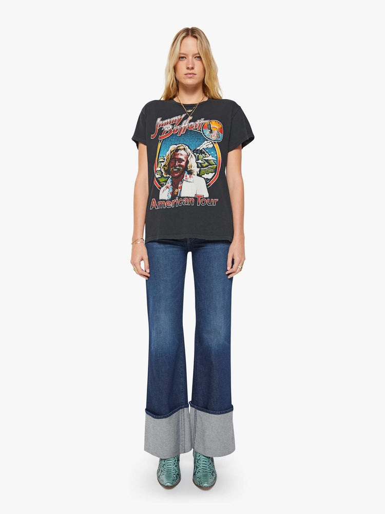 Full body view of a woman in a black tee is inspired by Jimmy Buffett's American tour merch with a graphic portrait on the front.