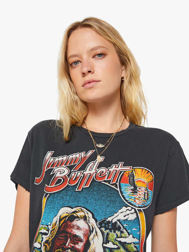 Close up view of a woman in a black tee is inspired by Jimmy Buffett's American tour merch with a graphic portrait on the front.