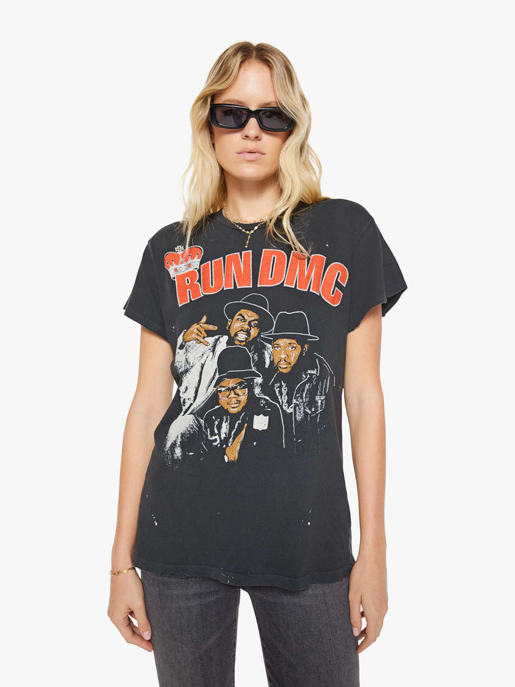 Front view of a woman in a black tee that pays homage to Run DMC with a graphic portrait on the front and text in white on the back.