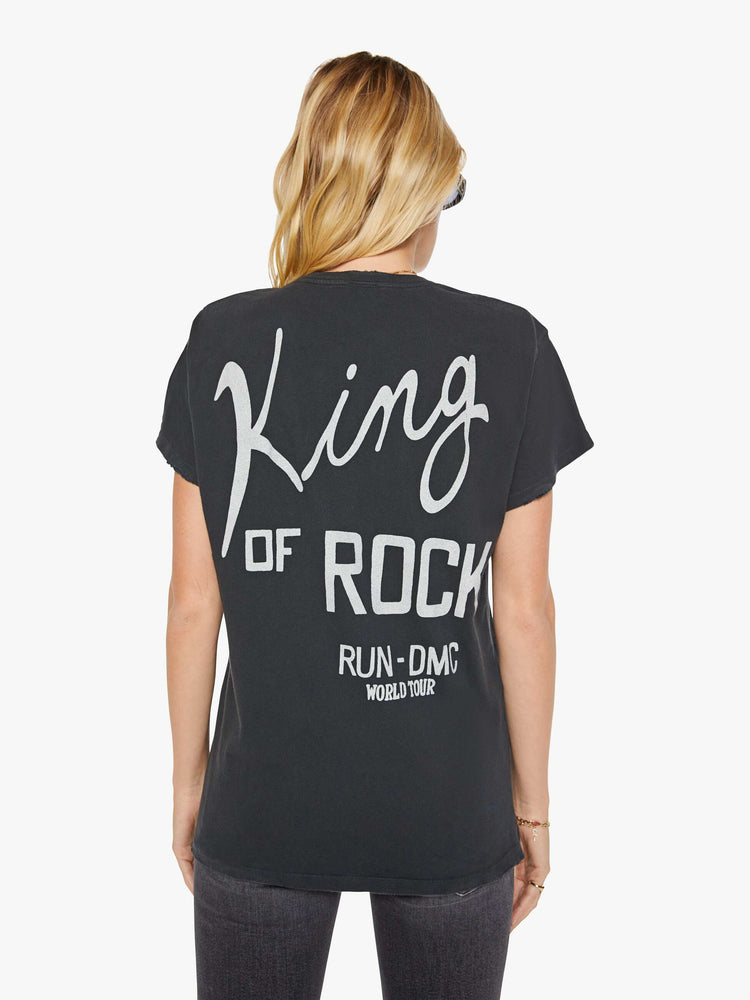 Back view of a woman in a black tee that pays homage to Run DMC with a graphic portrait on the front and text in white on the back.