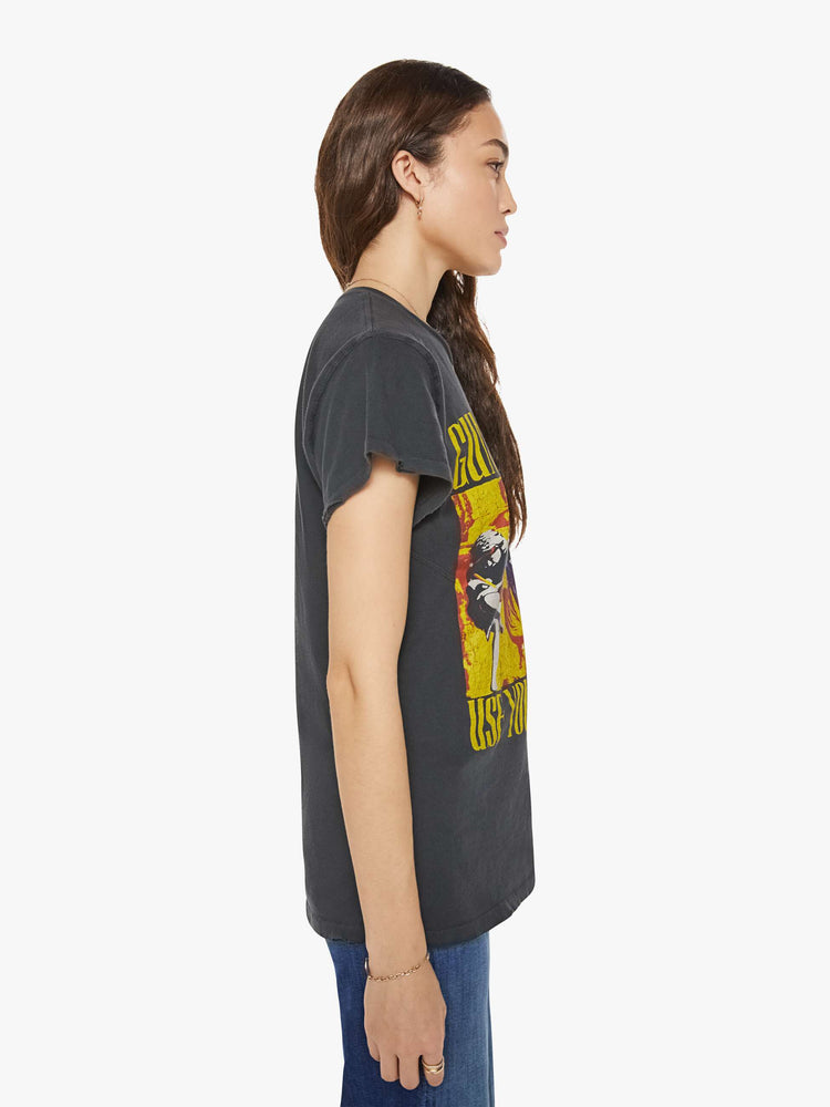 Side view of a woman in a black tee that homage to Guns N' Roses with a graphic portrait and text in yellow on the front.