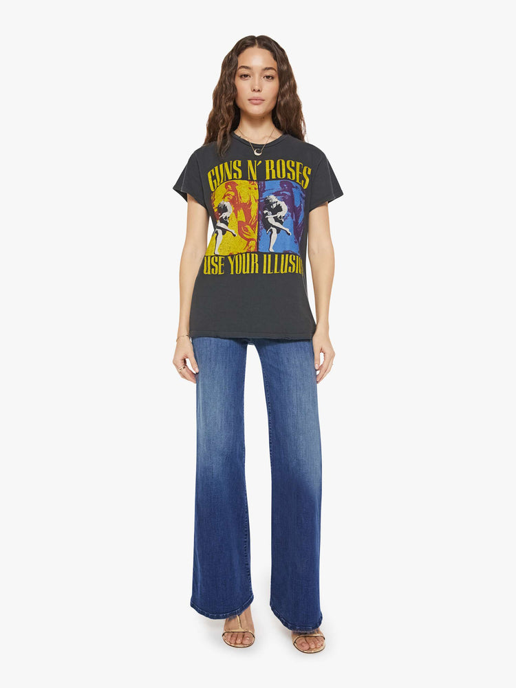 Full body view of a woman in a black tee that homage to Guns N' Roses with a graphic portrait and text in yellow on the front.
