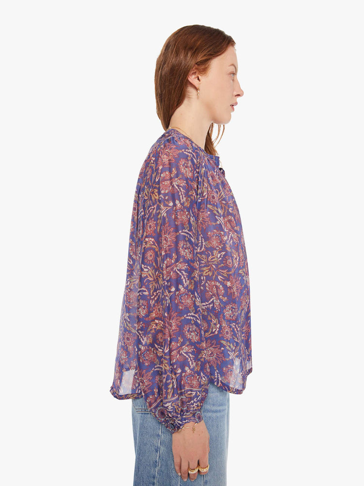 Side view of a woman in a shirt designed in a blue and pink floral print, and features a crew neck, long balloon sleeves and ruffles throughout for a flowy fit.