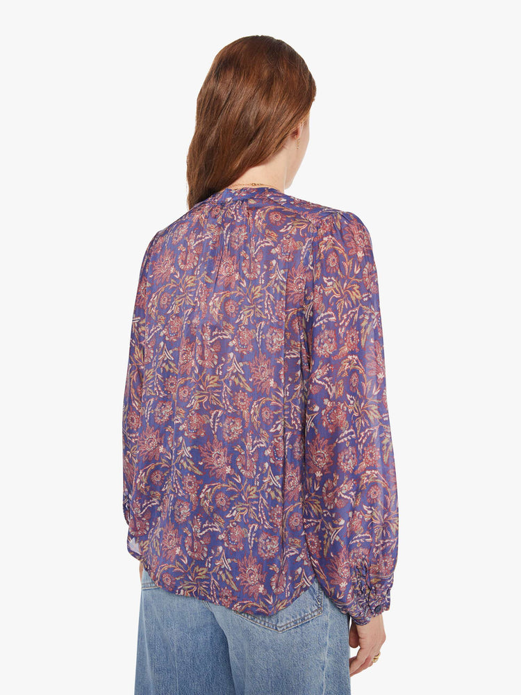 Back view of a woman in a shirt designed in a blue and pink floral print, and features a crew neck, long balloon sleeves and ruffles throughout for a flowy fit.
