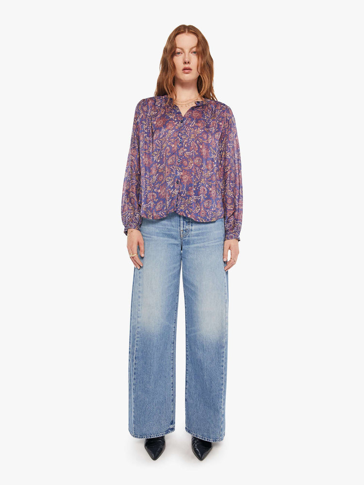 Full body view of a woman in a shirt designed in a blue and pink floral print, and features a crew neck, long balloon sleeves and ruffles throughout for a flowy fit.