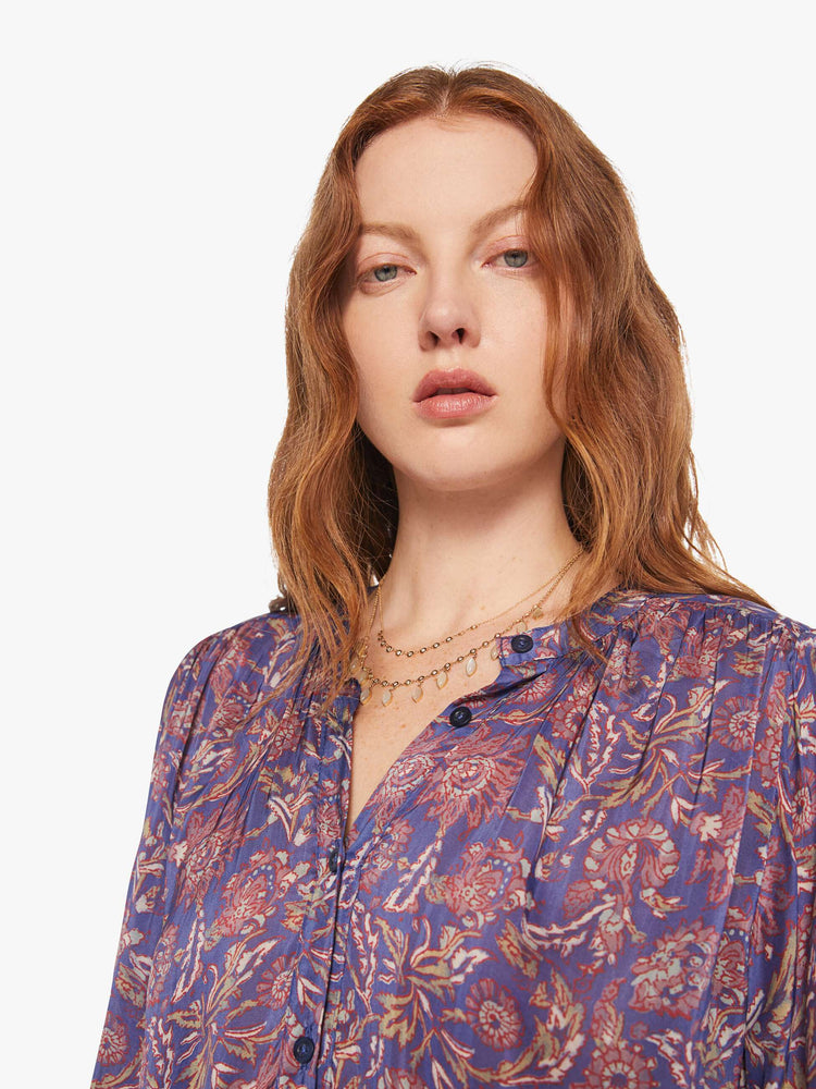 Close up view of a woman in a shirt designed in a blue and pink floral print, and features a crew neck, long balloon sleeves and ruffles throughout for a flowy fit.