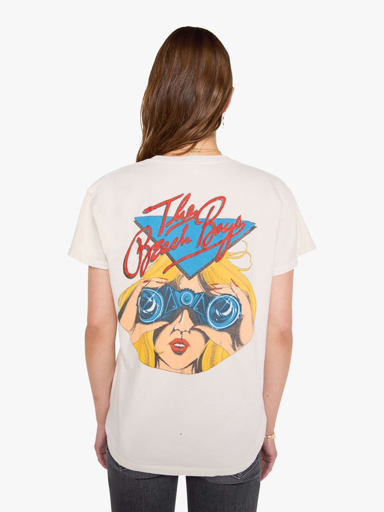 Back view of a woman in a off-white tee pays homage to The Beach Boys with a colorful graphic on the front and back.