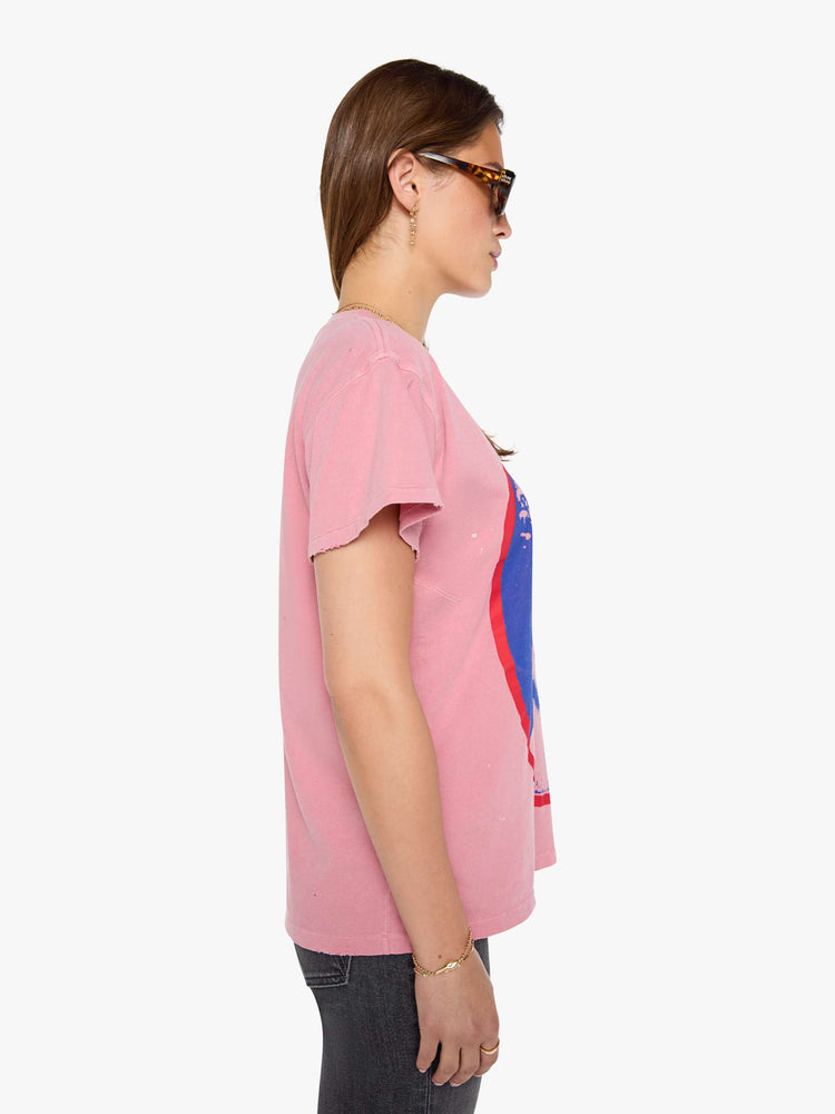 Side view of a woman in a pink tee pays homage to The Sex Pistols with a pop art-inspired graphic of the Queen of England in blue and red on the front. 