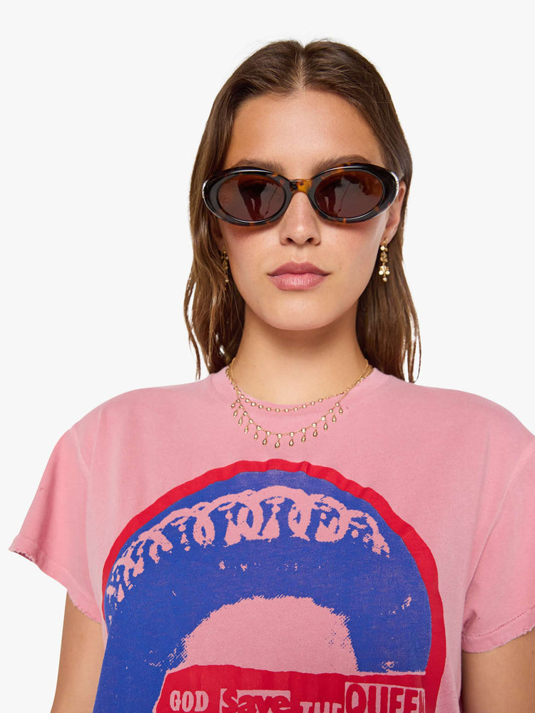 Close up view of a woman in a pink tee pays homage to The Sex Pistols with a pop art-inspired graphic of the Queen of England in blue and red on the front. 