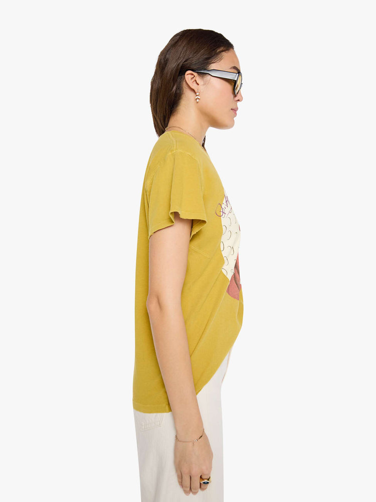 Side  view of a woman in a yellow yellow the tee honors Devo with a graphic portrait and colorful text on the front.
